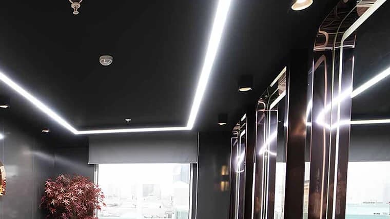 Salle aux murs sombres et bandeaux lumineux au plafond, avec de grandes fenêtres et des postes à miroirs