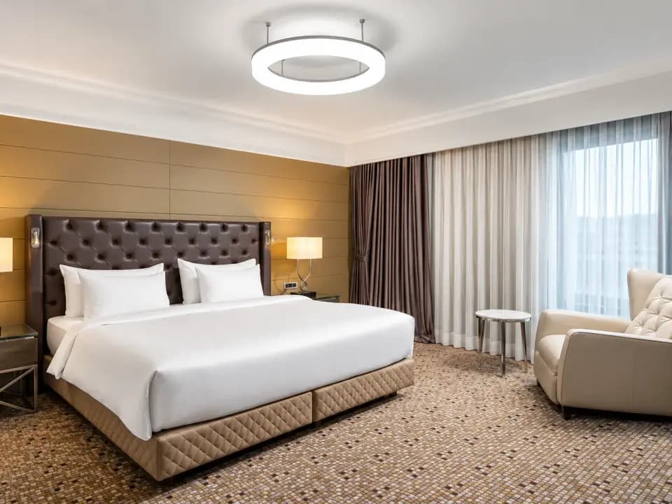 Chambre d'hôtel avec lit double, tête de lit capitonnée, fauteuil et rideaux tirés
