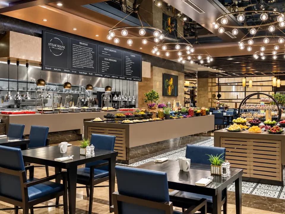 Salle du petit-déjeuner avec buffet garni, tables dressées et banquettes bleues