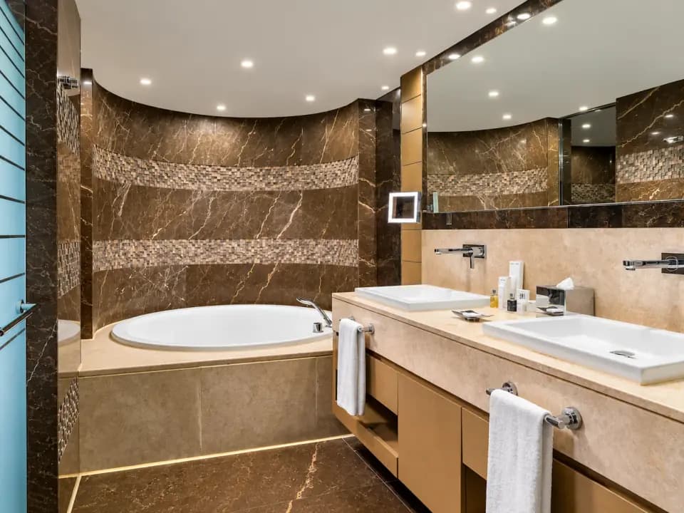 Salle de bain en marbre beige avec baignoire encastrée, double vasque et grands miroirs